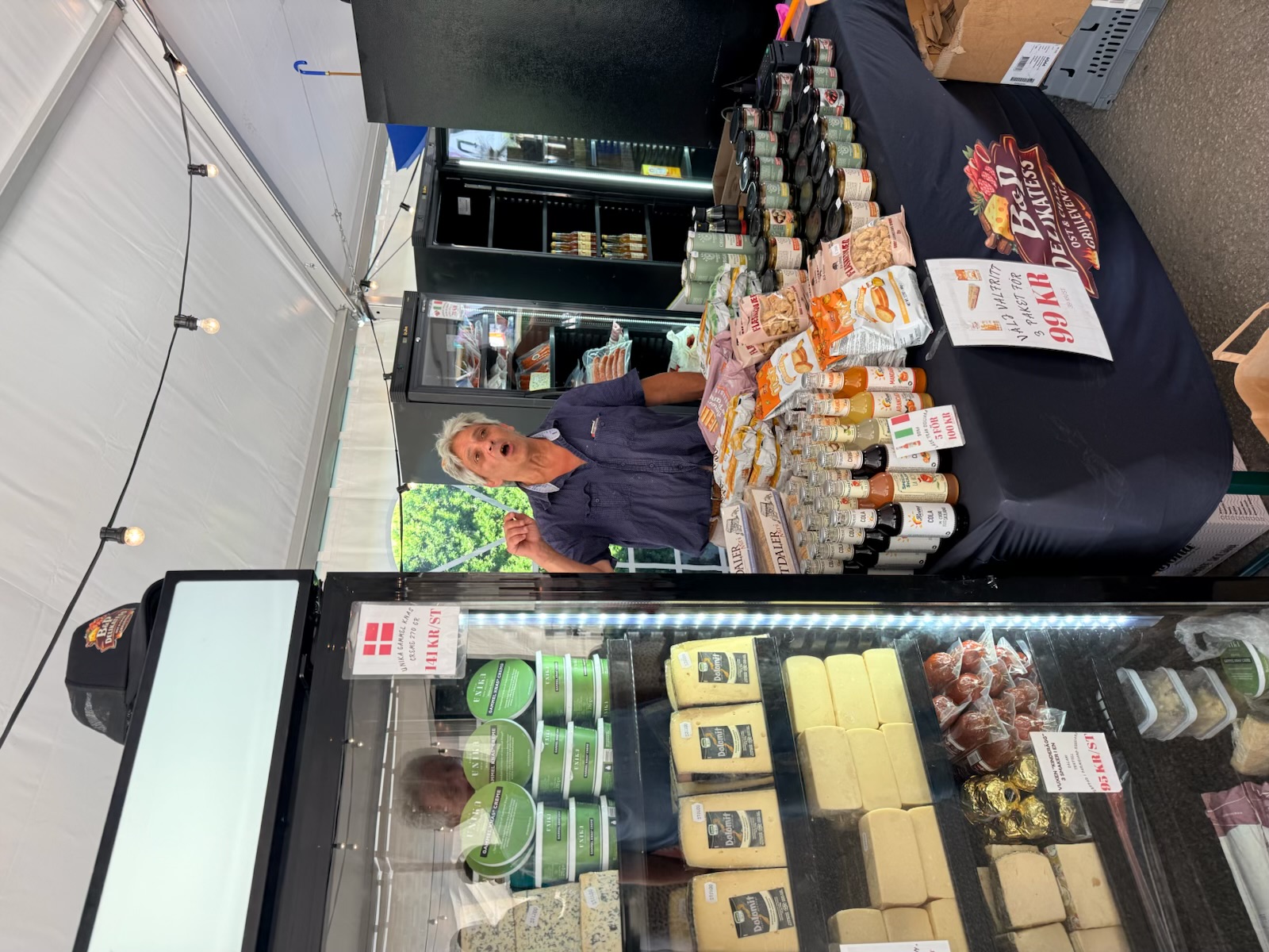 Paul bakom B&P Delikatess marknadsdisk med ostar, drycker och delikatesser